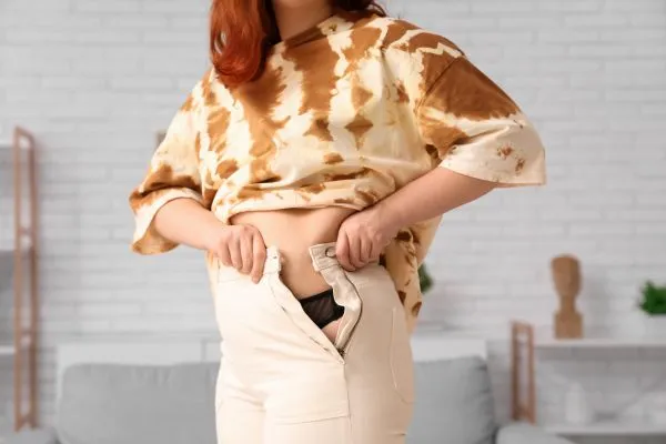Image of woman trying to do her trousers up after pregnancy weight gain Small Heath