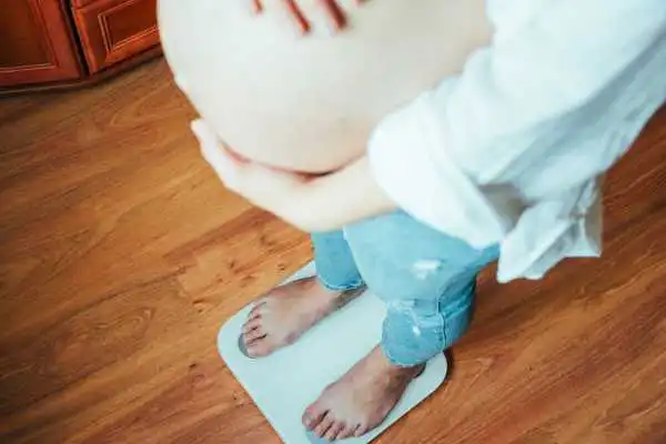 Image of woman weighing herself and experiencing weight gain through pregnancy Small Heath